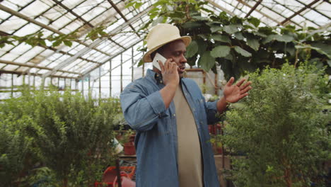 Black-Farmer-Going-through-Greenhouse-and-Speaking-on-Phone
